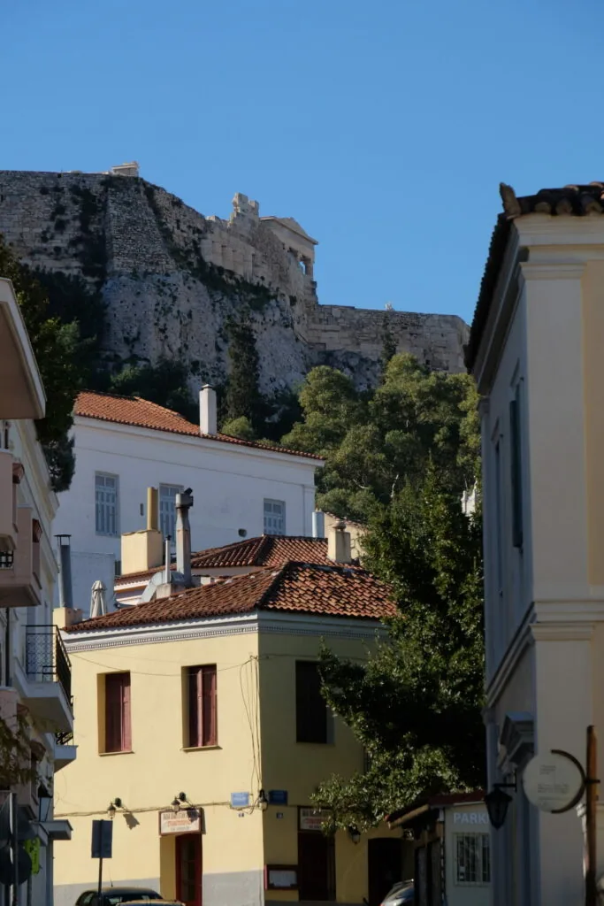 Narrow street with yellow and white buildings beneath a historic fortress on a hillside against clear blue sky