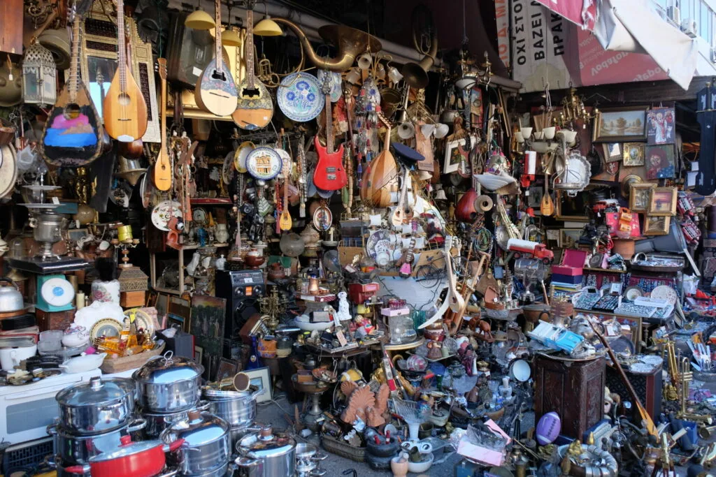 Crowded shop storefront displaying hundreds of vintage items including musical instruments, decorative plates, cookware, and collectibles hanging from walls and ceiling