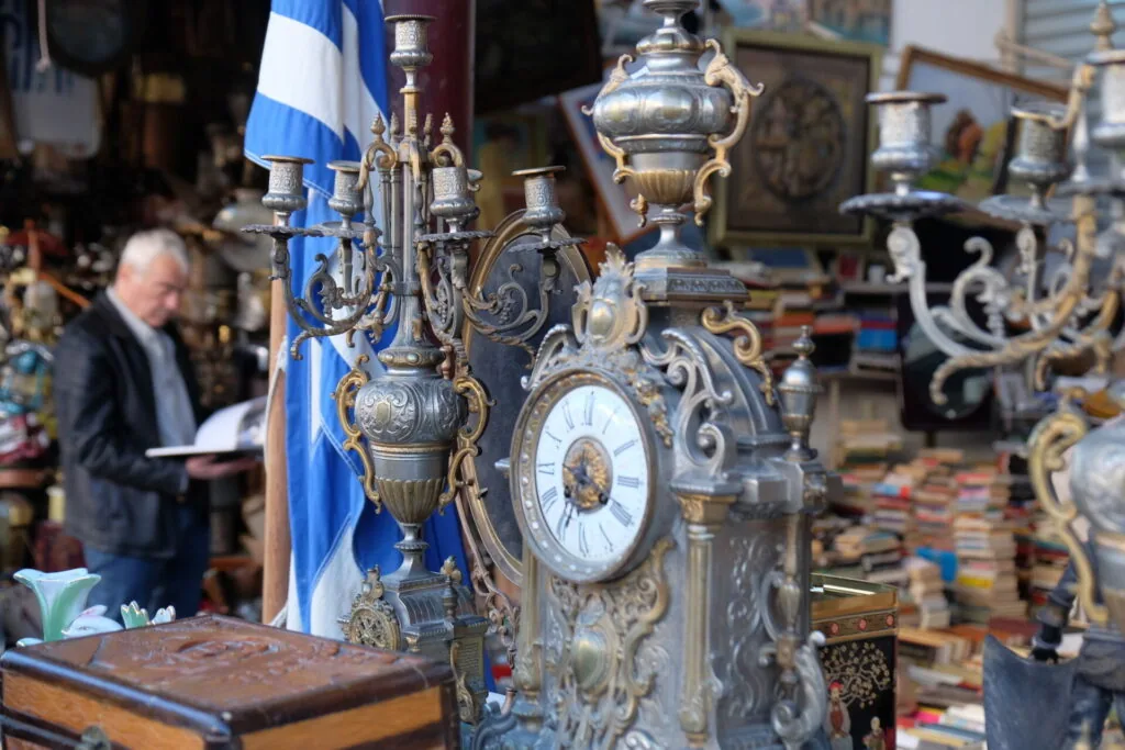 Ornate antique brass clock with decorative candelabra and blue flag in cluttered shop with person examining items