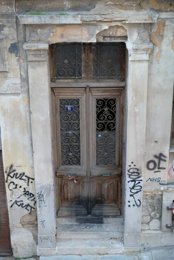 Weathered wooden door with ornate iron grilles set in deteriorating stone facade, marked with graffiti
