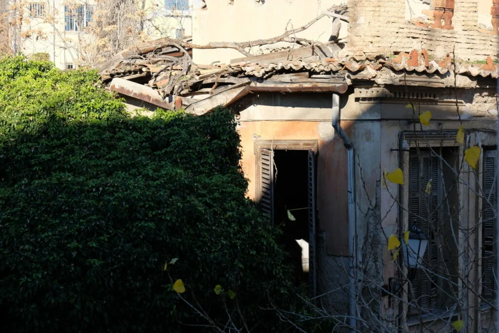 Dilapidated building with collapsed roof, ivy-covered walls, and overgrown vines covering weathered structures.