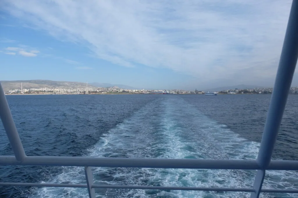View from boat showing coastal city skyline across blue water with wake trail behind vessel