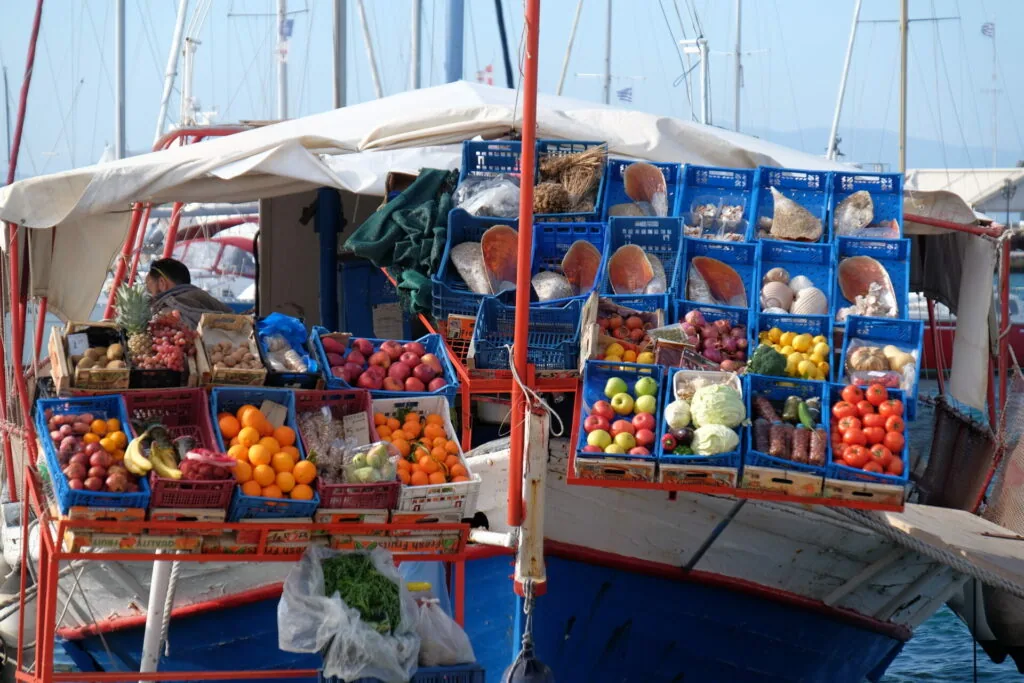 Fishing boat loaded with fresh produce in blue and red crates, displaying tomatoes, oranges, and vegetables for sale at a harbor