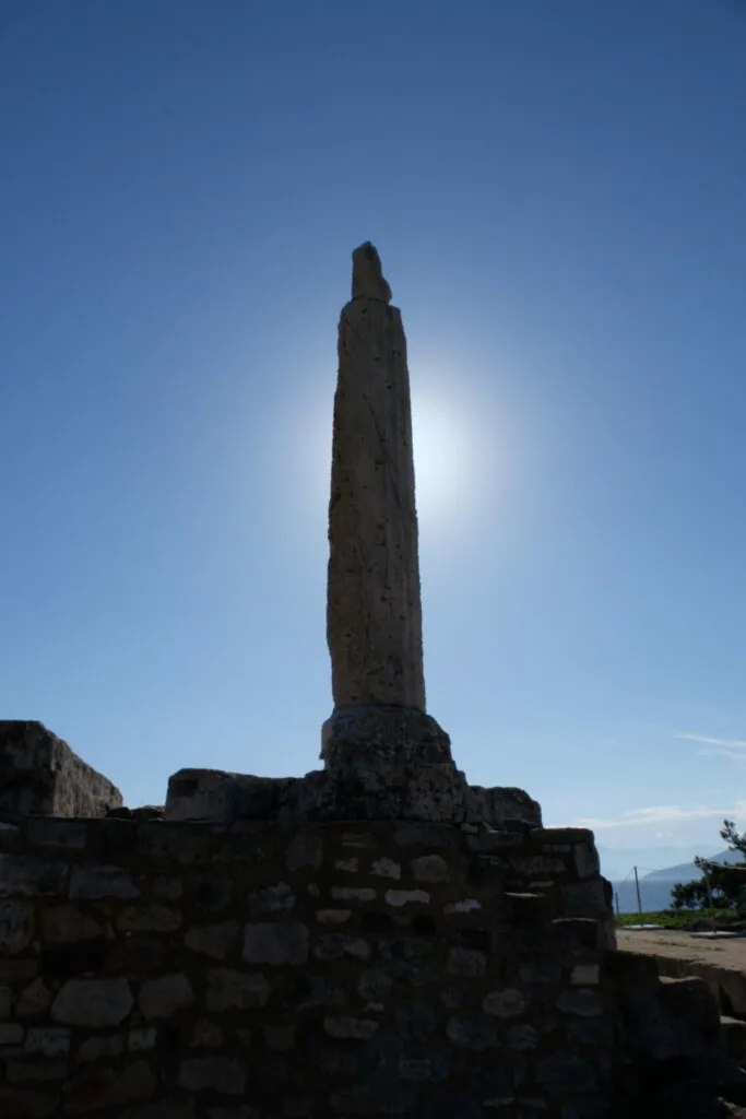 Tall stone obelisk monument standing on a stone base against a clear blue sky