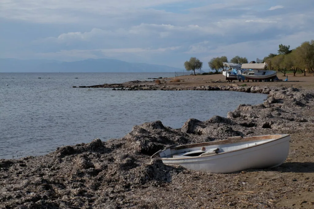Small white rowboat beached on rocky shore with mountains visible across calm blue water