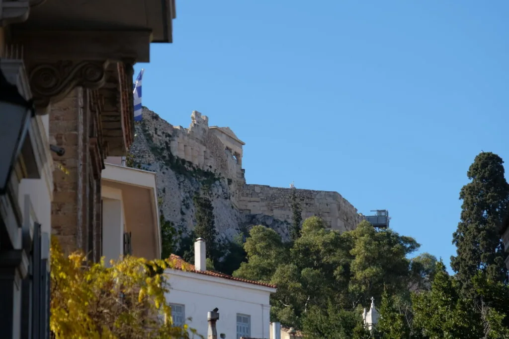 Ancient stone fortress overlooking white buildings with ivy-covered walls and green vegetation under clear blue sky