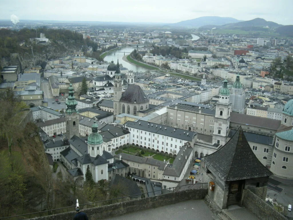 Aerial view of European riverside city with church domes, mountains, and curved waterway through urban landscape