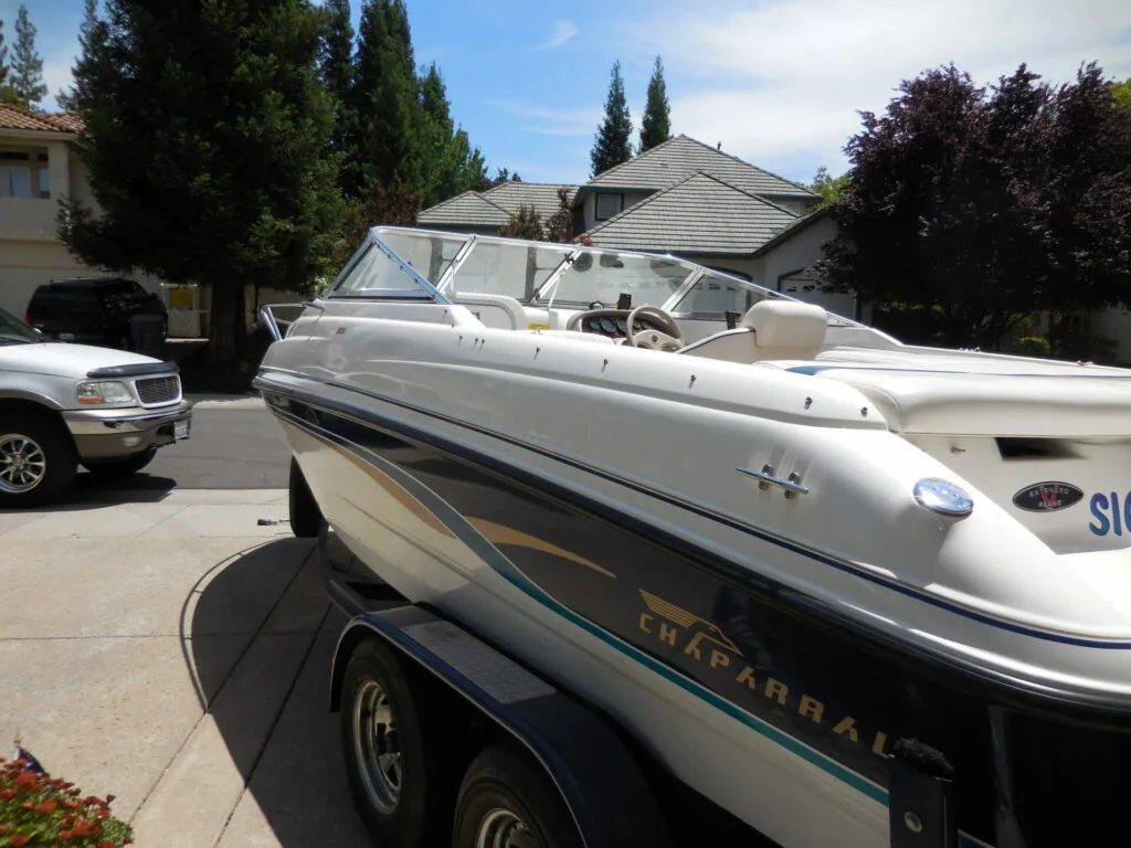 White speedboat with tan interior on dual-axle trailer in residential driveway