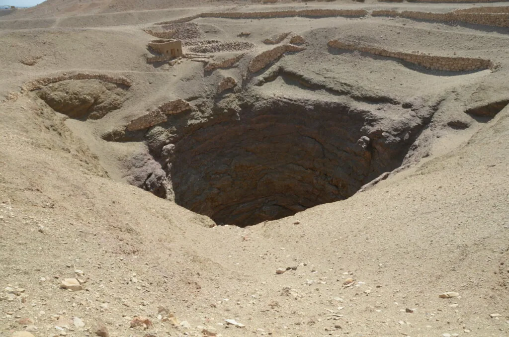 Archaeological excavation pit with exposed stone foundations and mud brick structures in desert sand