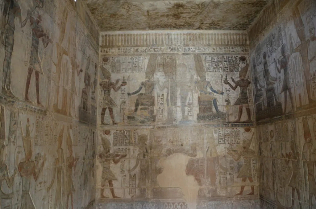Ancient Egyptian tomb interior with faded hieroglyphics and figures painted on stone walls and ceiling