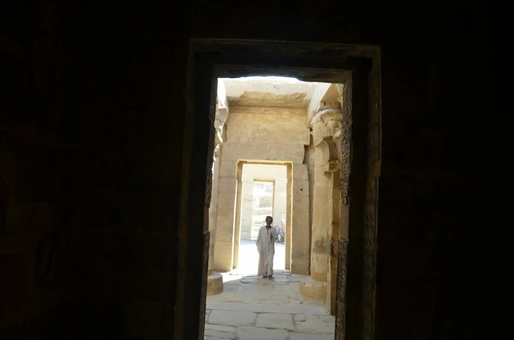 Person in light clothing standing in doorway of ancient stone corridor with successive rectangular openings creating depth perspective