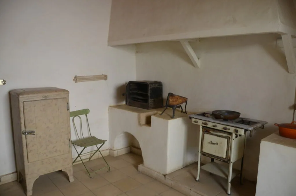Vintage kitchen interior with beige refrigerator, folding chair, shelving, stove, and cookware