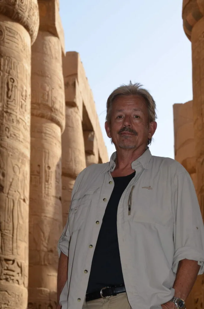 Man in light-colored shirt standing between ancient carved stone columns with hieroglyphics