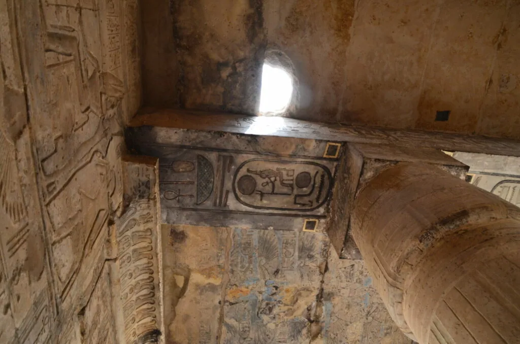 Ancient Egyptian temple interior with hieroglyphic carvings on walls and a shaft of light from above.