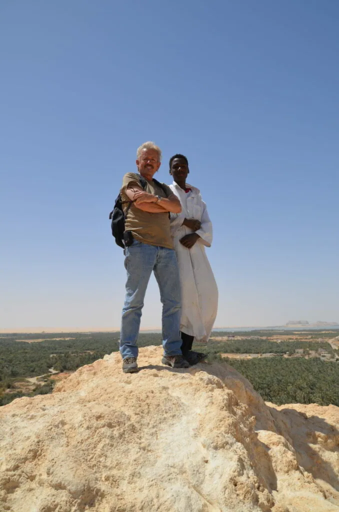 Two people standing together on a rocky outcrop overlooking a vast agricultural valley under clear blue sky