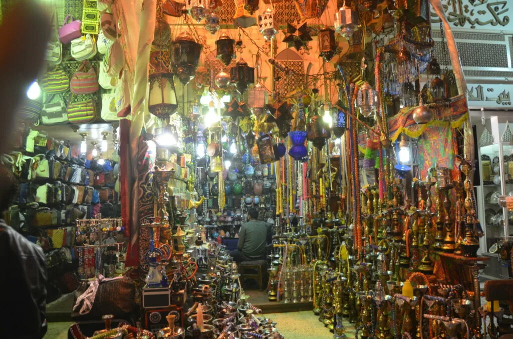 Narrow marketplace stall densely packed with hanging ornaments, lanterns, and decorative items illuminated by warm lighting