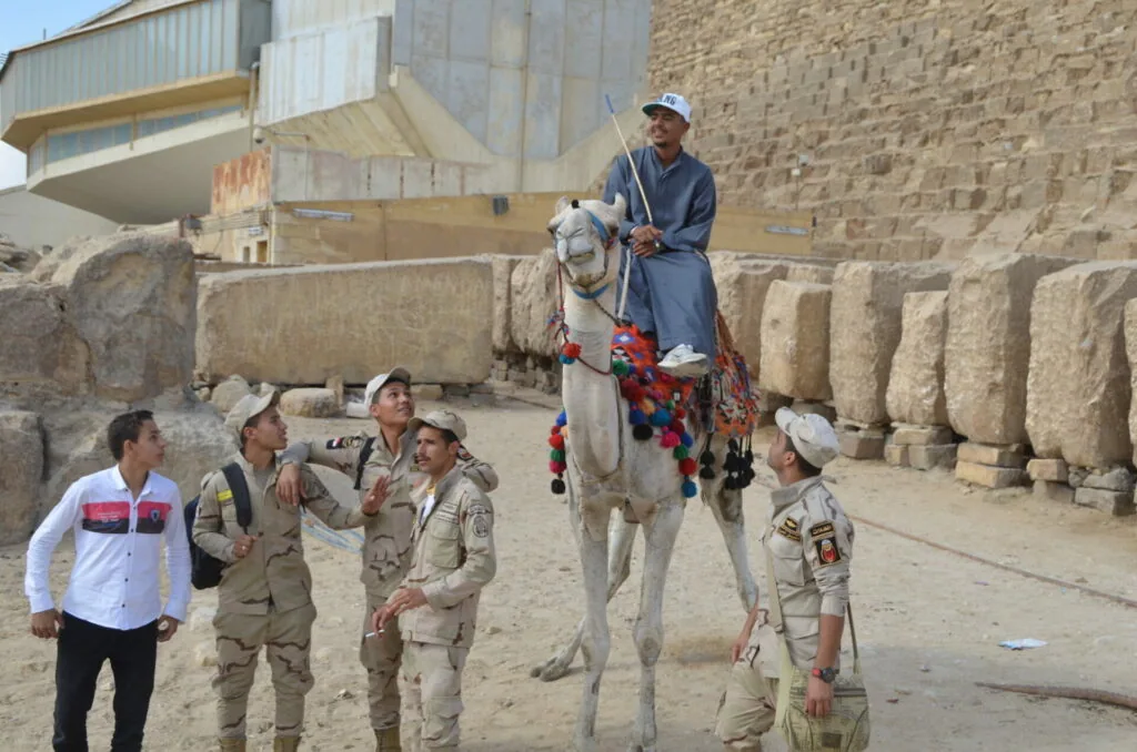 Man riding decorated camel with group of people in desert setting near stone structures