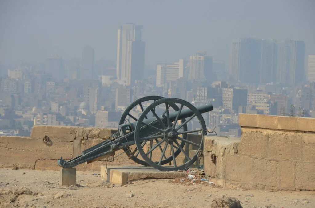 Vintage cannon on stone fortification overlooking hazy cityscape with high-rise buildings
