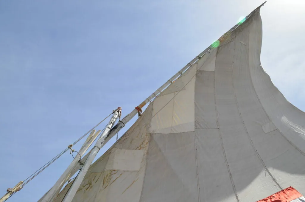 Worker climbing rigging on large white sail against blue sky