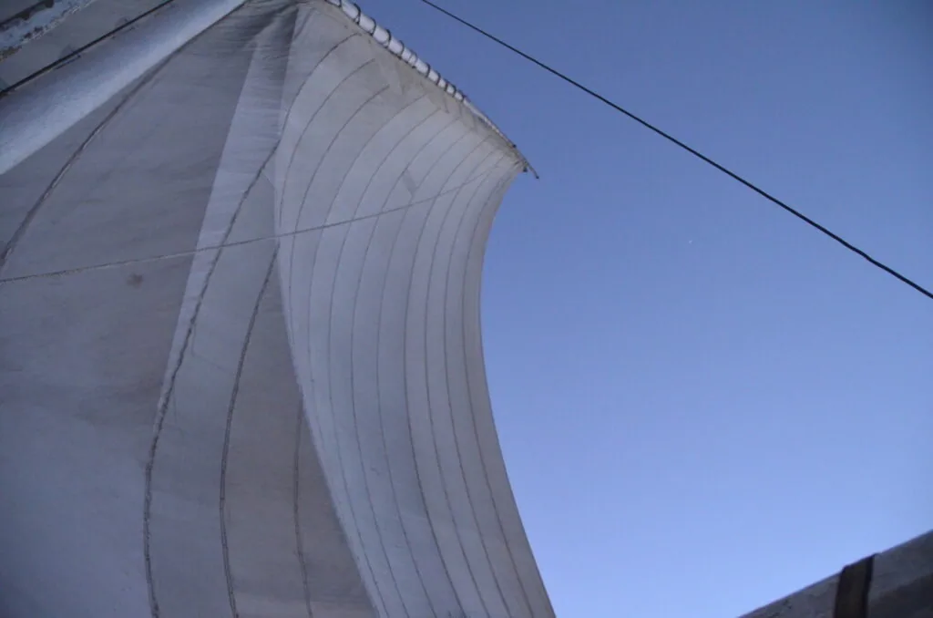 White sail billowing against clear blue sky with rigging visible