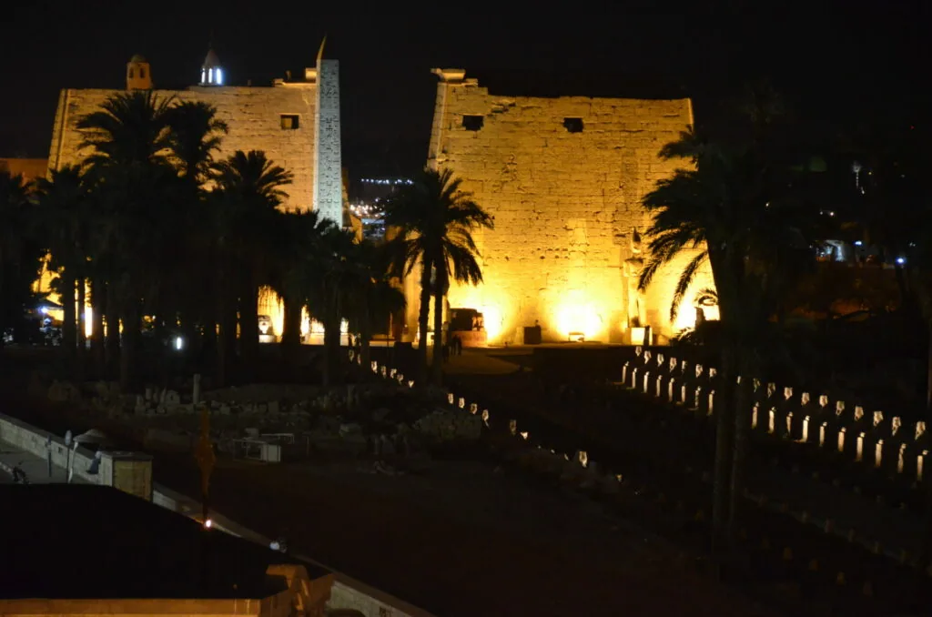 Illuminated ancient stone fortress towers with palm trees at night