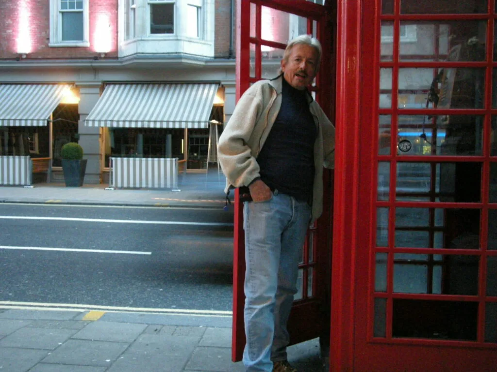 Man standing beside red telephone booth on city street at dusk