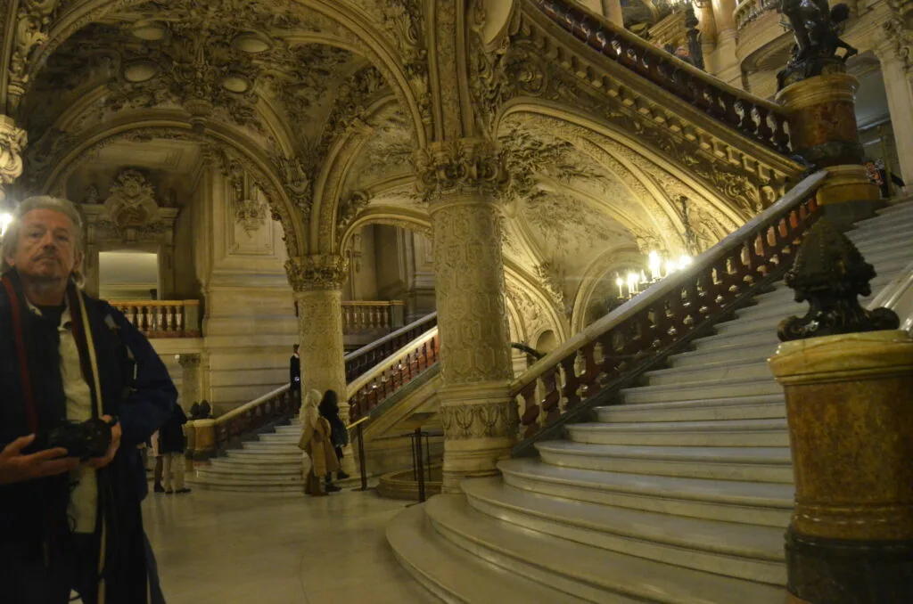 Grand ornate staircase with carved columns, gilded ceiling details, and white marble steps in a classical European palace interior