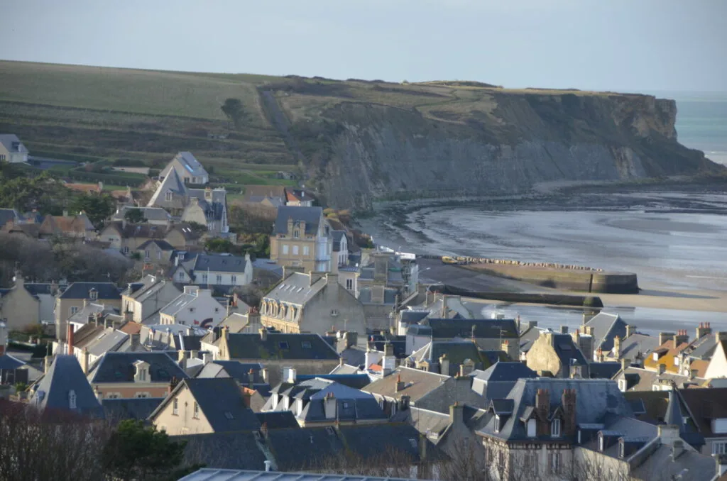 Coastal town with stone buildings and church nestled below dramatic chalk cliffs, sandy beach and harbor visible