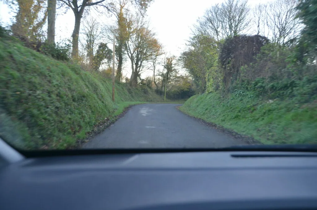 Narrow tree-lined country road with steep moss-covered banks viewed from inside a vehicle