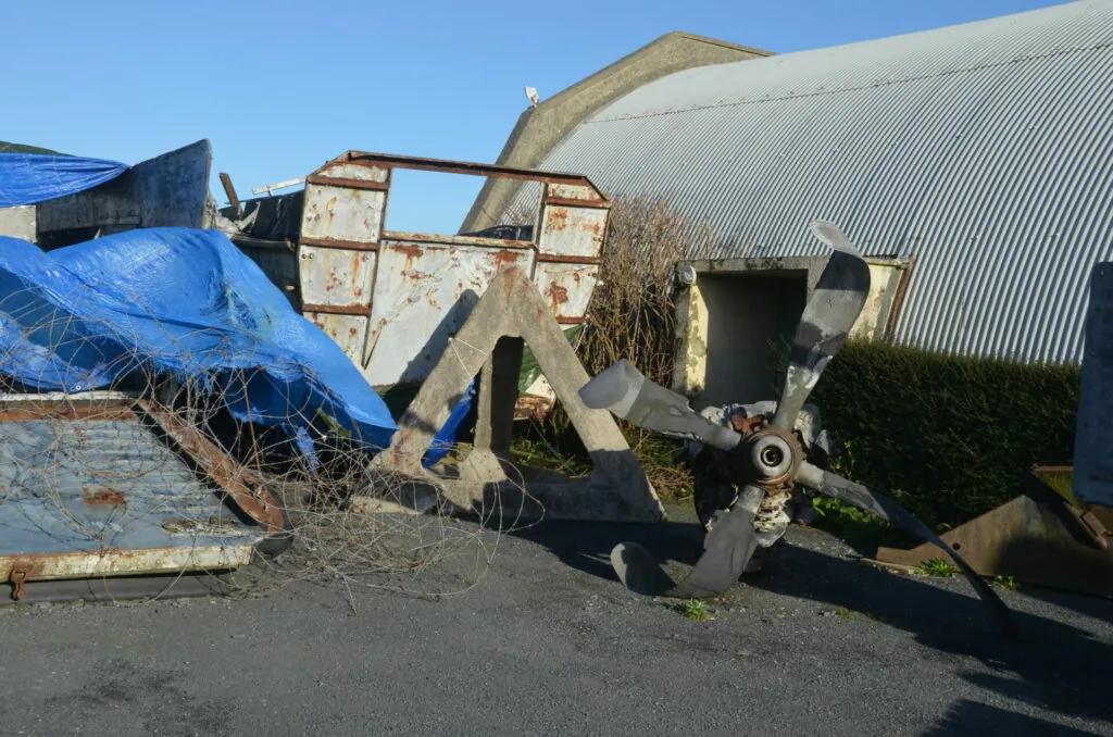 Abandoned rusted farm equipment and machinery scattered outside weathered industrial buildings with corrugated metal siding