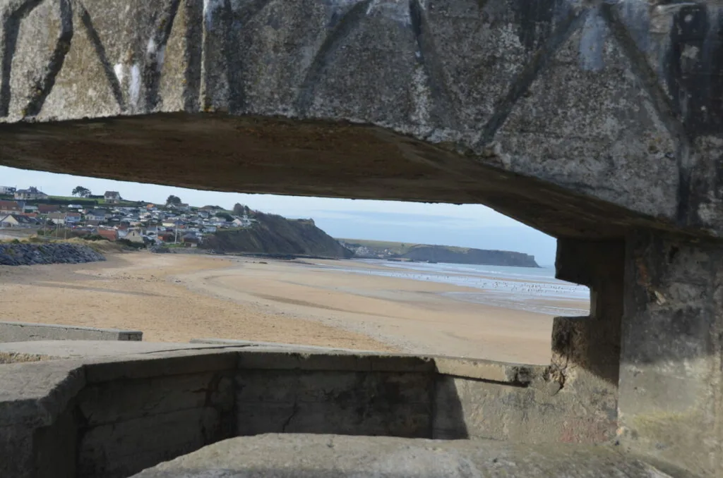 Coastal beach view through weathered concrete structure with houses on cliffs in background
