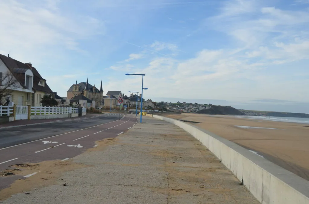 Seaside promenade with street lamp, white barrier wall, beach, and Victorian architecture buildings under blue sky