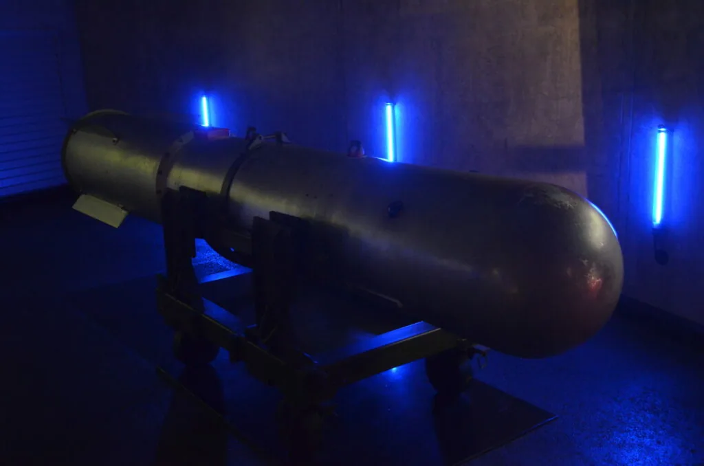 Dark cylindrical missile or rocket displayed on a stand with bright blue neon lighting in background