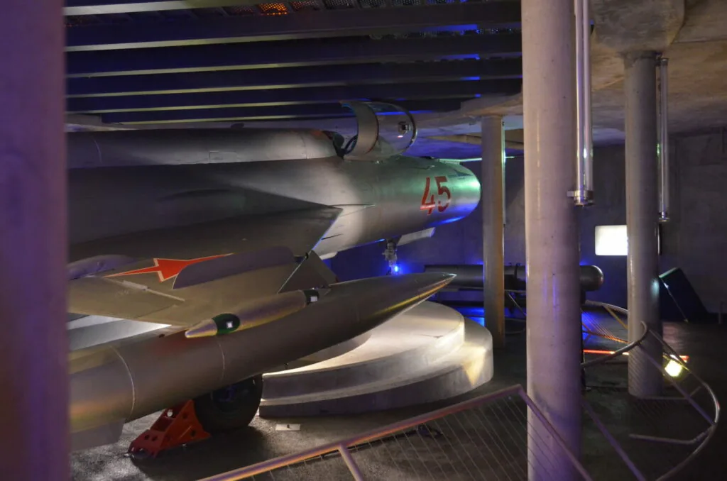 Aircraft fuselage sections displayed in museum under blue lighting with structural supports and red accents