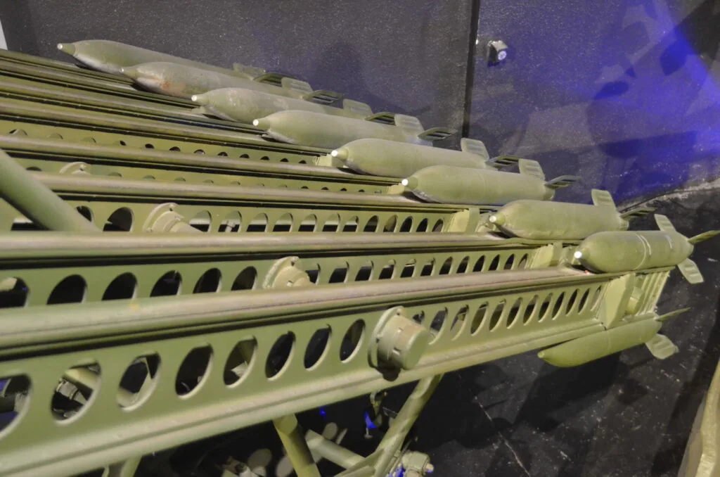 Pale yellow-green industrial rail or track system with perforated panels and cylindrical connectors, photographed indoors under blue lighting