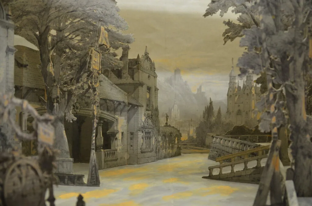 Medieval stone village street with ornate trees, historic buildings, and castle towers in misty distance