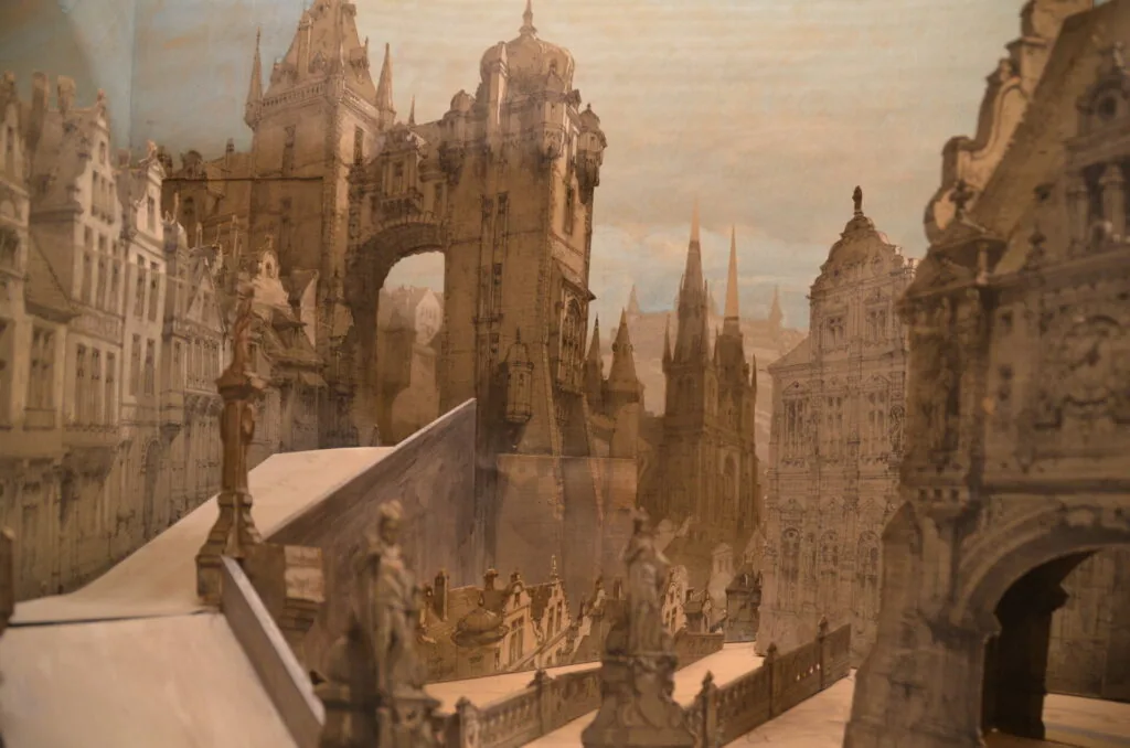 Detailed architectural model of a medieval European city featuring ornate Gothic towers, spires, and buildings in tan stone.