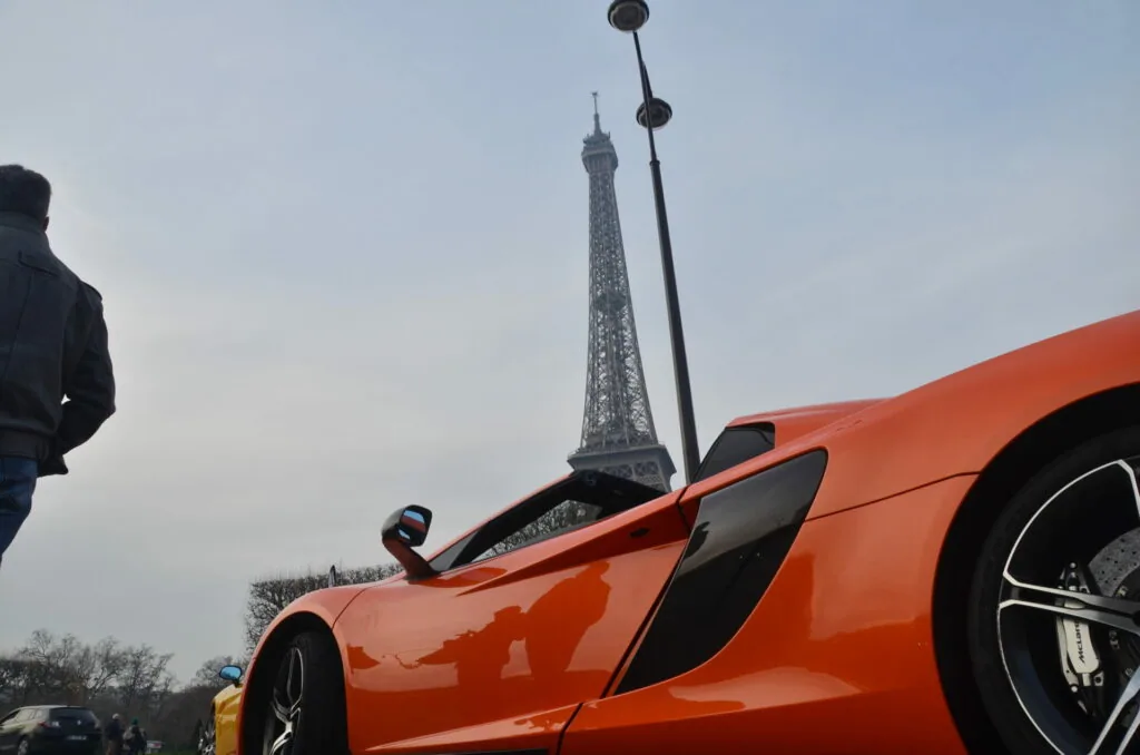 Orange sports car parked with Eiffel Tower in background under cloudy sky