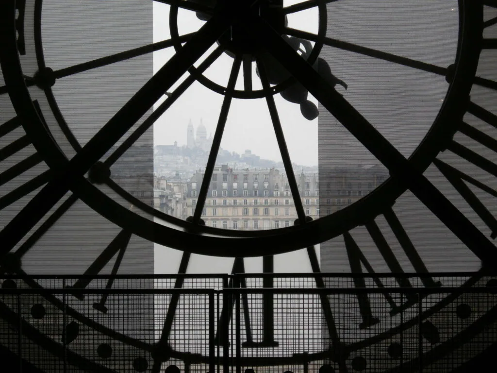 View of Parisian cityscape and buildings through silhouetted clock face with Roman numerals
