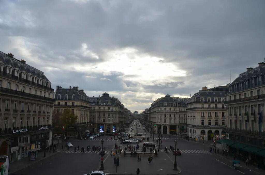 Parisian avenue with ornate Haussmann-style buildings, pedestrians, and cloudy sky