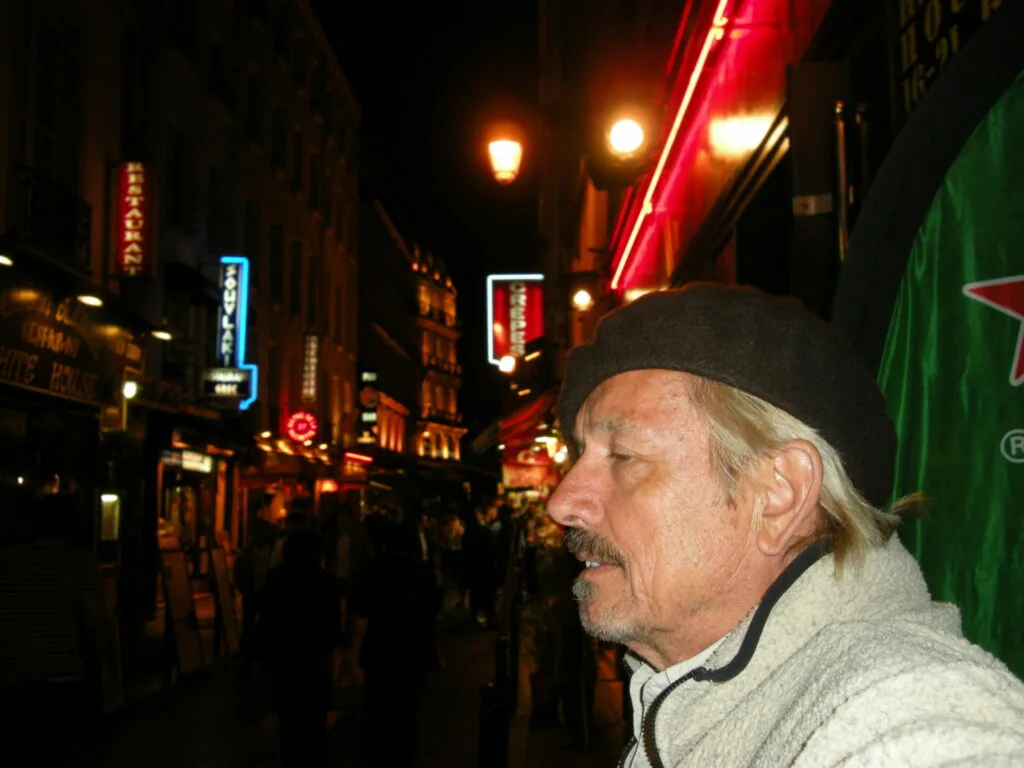 Man wearing black cap and light jacket on illuminated nighttime street with neon signs