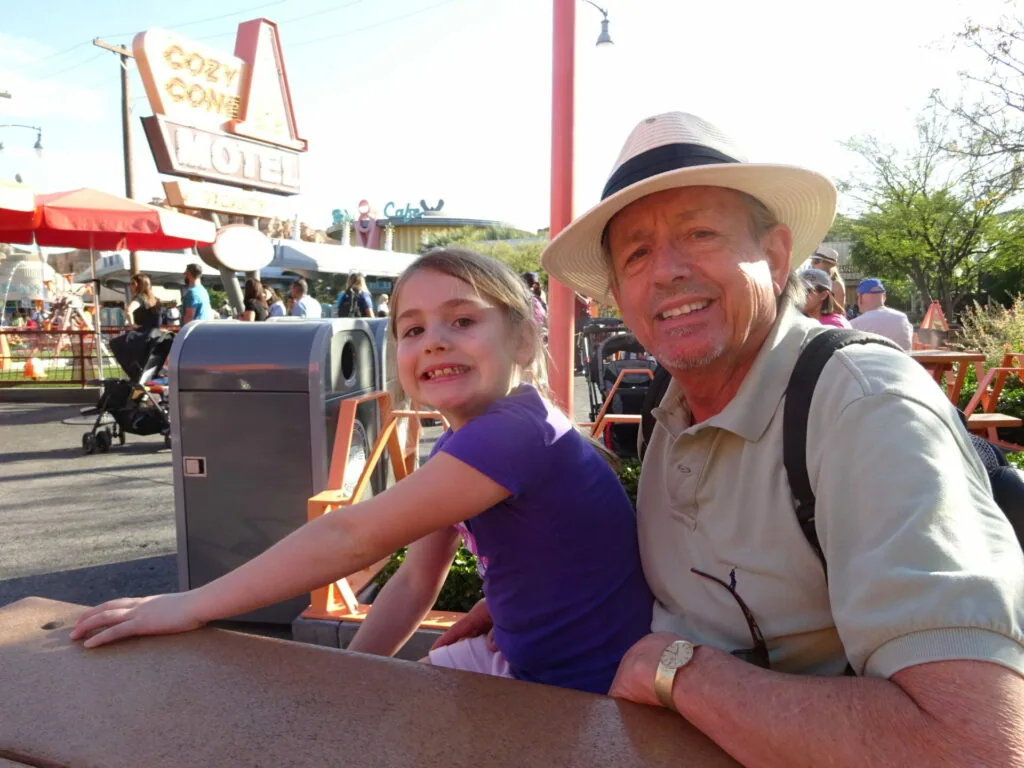 Adult and child smiling at amusement park counter with vintage signage and rides in background