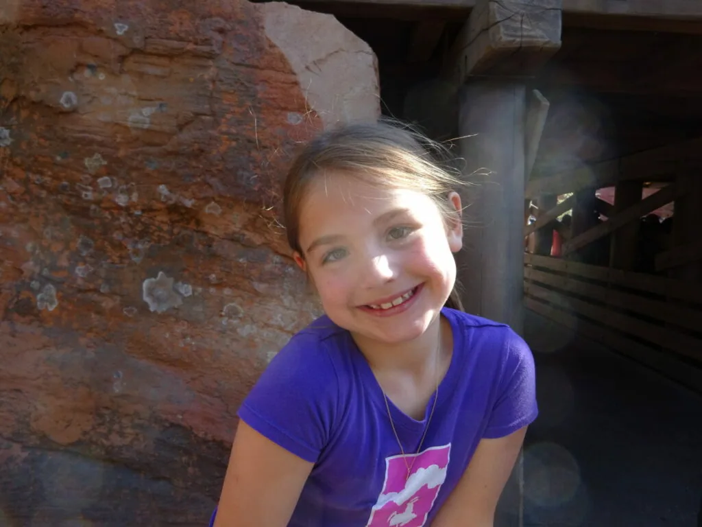 Smiling child in purple shirt standing against weathered brick wall