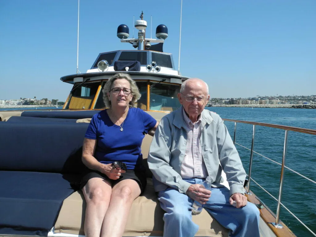 Two people sitting on a luxury yacht with coastal homes visible across the blue water