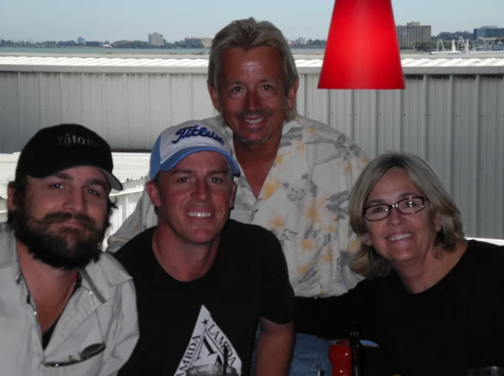 Four people posing together at an indoor venue with waterfront view and red pendant lamp