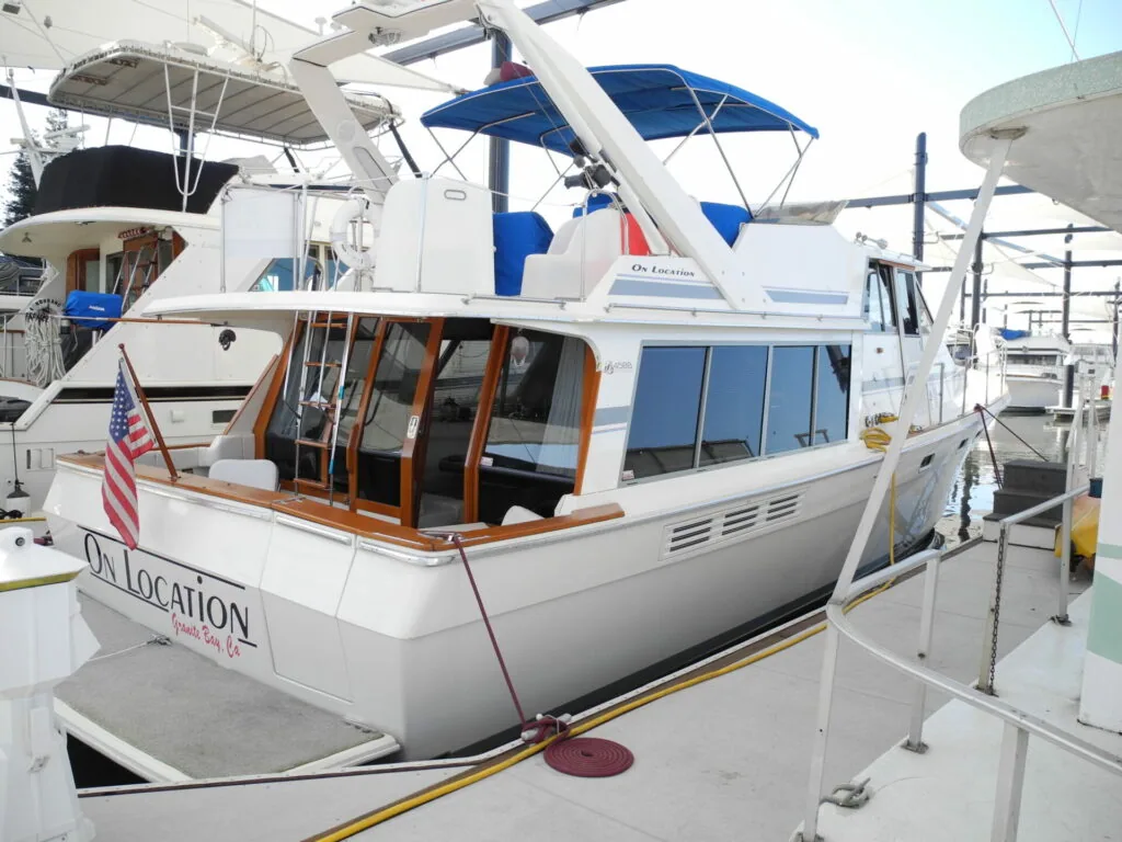 White motor yacht with blue canopies docked at marina, American flag visible on stern