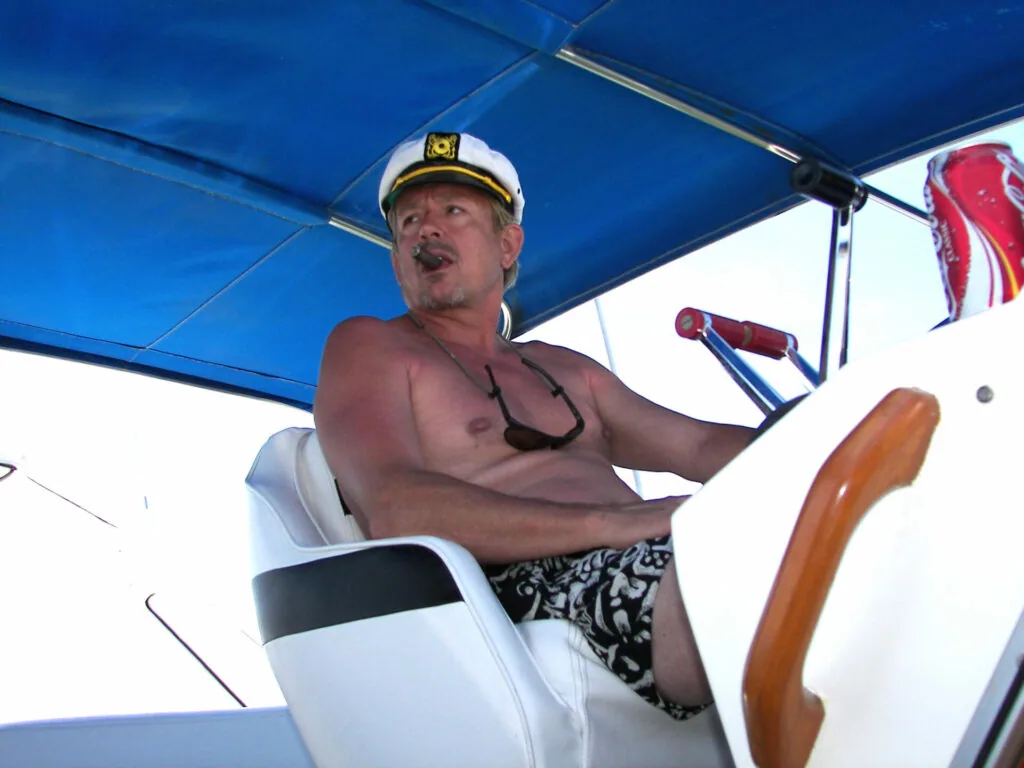 Man in captain's hat steering a boat under blue canopy