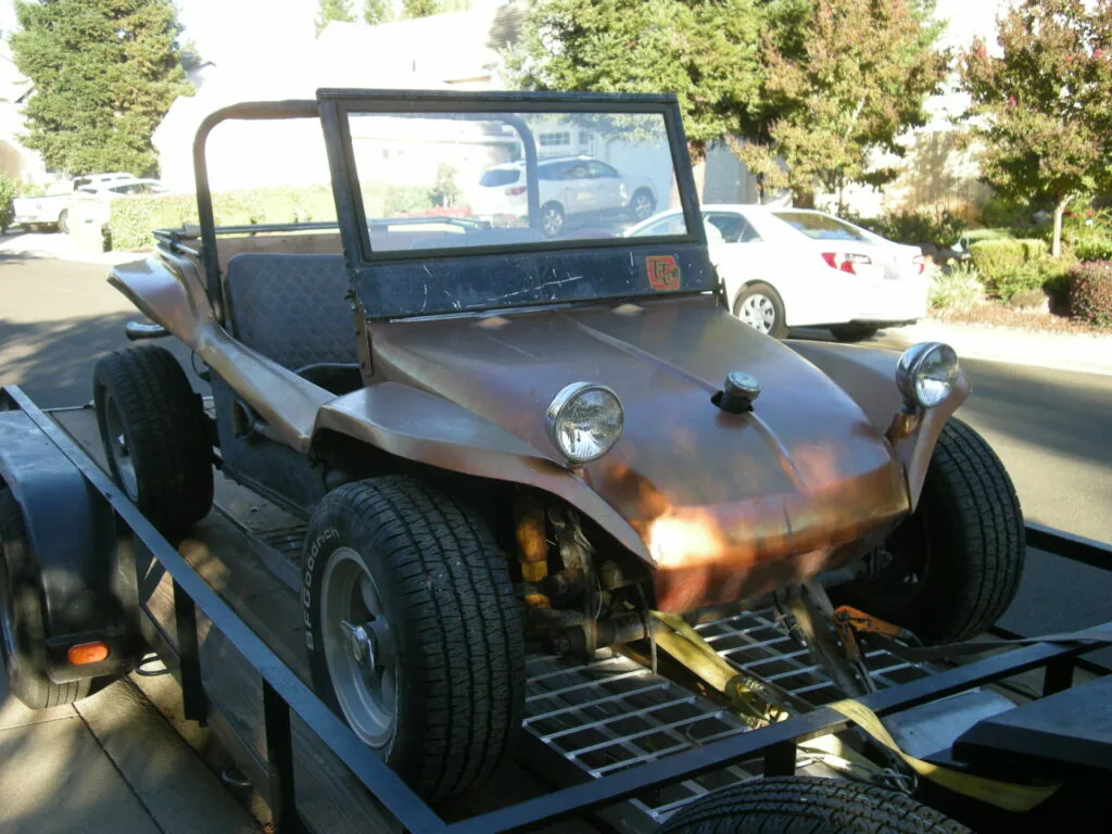 Custom-built dune buggy with exposed frame and open sides being transported on a flatbed trailer