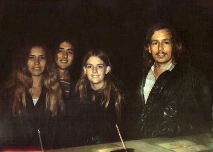 Four people with long hair posing together against a dark background