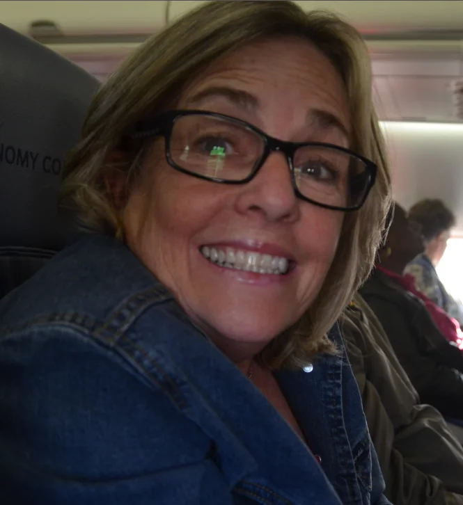 Woman wearing glasses and denim jacket smiling at camera inside an aircraft